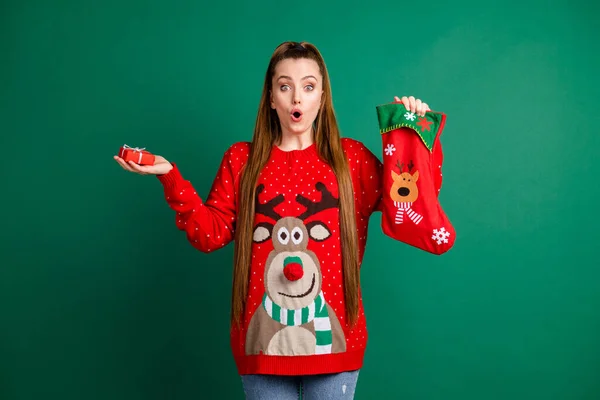 Fotografie šokované okouzlující dáma držet novoroční punčocha dárek malý dárek balíček otevřených úst nečekané překvapení nosit červené ošklivé ornament jelena pulovr izolované zelené barvy pozadí — Stock fotografie
