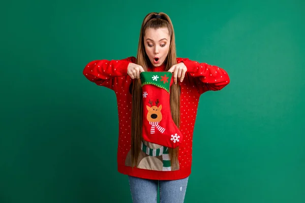 Photo of attractive shocked lady hold newyear stocking x-mas present family tradition look inside open mouth long-waited gift wear red ugly ornament pullover isolated green color background — Stock Photo, Image