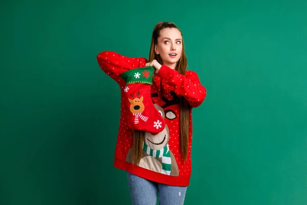 Photo of attractive funny pretty lady hold newyear stocking x-mas morning take her present family tradition exchange curious expression wear red ugly pullover isolated green color background — Stock Photo, Image