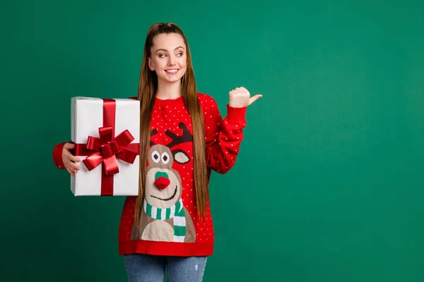 Photo of attractive charming lady newyear party hold large giftbox present pack direct thumb finger look side empty space x-mas novelty wear red ugly pullover isolated green color background — Stock Photo, Image