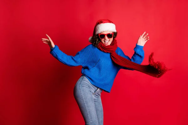 Фотопортрет молодої жінки, яка танцює на новорічній вечірці в окулярах шарф Санта-капелюх синій светр ізольований на яскраво-червоному фоні — стокове фото