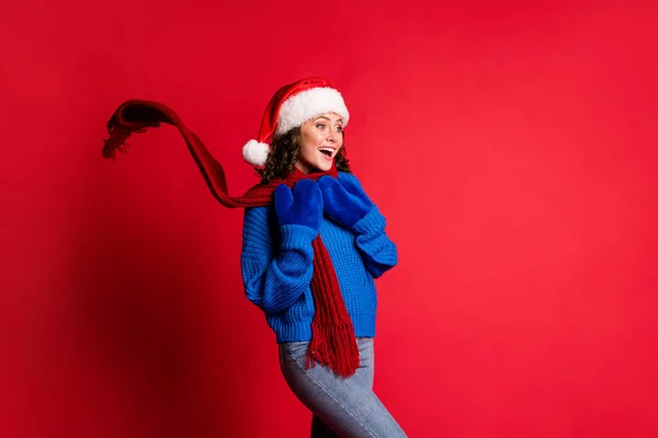 Zdjęcie portret zadowolony zaskoczony dziewczyna trzymając się za ręce do klatki piersiowej otwarte usta płynący szalik noszenie santa kapelusz niebieski pullover izolowane na jasnoczerwonym tle — Zdjęcie stockowe