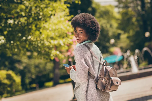 Foto van positieve donkere huid dame houden smartphone dragen rugzak reizen in de buitenlucht lente bos stad park — Stockfoto