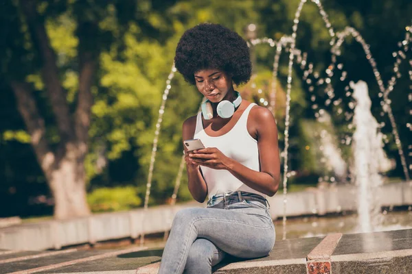 Afro-Amerikalı kızın fotoğrafı mermer taşlı çeşmede oturur ve Spring Town Center Park 'ta sosyal ağ haberleri okur. — Stok fotoğraf