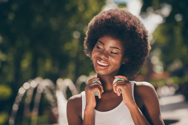 Portret van een charmant Afrikaans meisje dat haar draadloze headset aanraakt in het zomerstadspark met fonteinen — Stockfoto