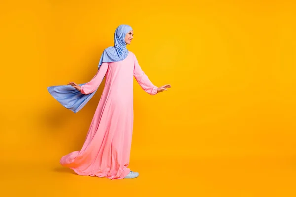 Comprimento total do corpo tamanho vista de muslimah muito alegre vestindo vestido hijab olhando para o lado andando cópia espaço isolado brilho cor amarela fundo — Fotografia de Stock