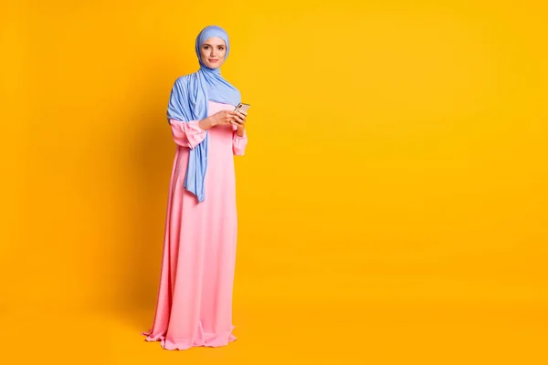 Comprimento total do corpo tamanho vista de agradável muito elegante muslimah vestindo vestido hijab usando dispositivo blog isolado no fundo de cor amarela brilhante — Fotografia de Stock