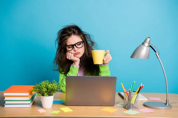 Jag behöver mer kaffe. Utmattad flicka sitta skrivbord arbete fjärr utseende håll koffein dryck mugg isolerad blå färg bakgrund — Stockfoto