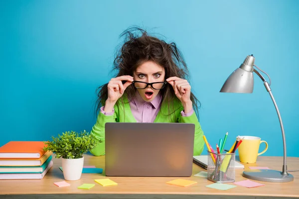 Foto van verbaasd meisje zitten tafel werk remote look laptop touch specs dragen groen shirt geïsoleerd op blauwe kleur achtergrond — Stockfoto
