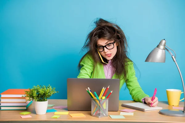 Porträtt av överarbetad flicka sitta bord arbete laptop skriva anteckning bok bära grön skjorta isolerad på blå färg bakgrund — Stockfoto