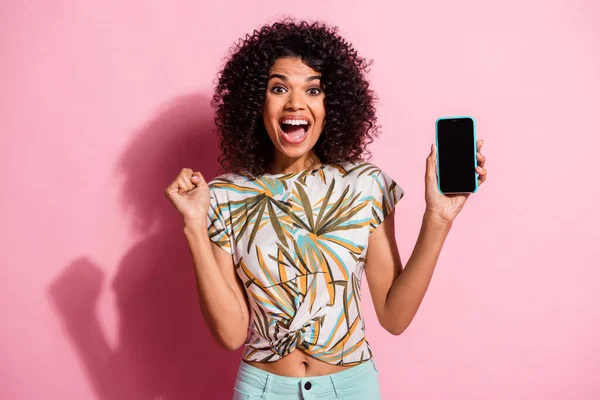 Foto retrato de una mujer celebrando sosteniendo el teléfono con espacio en blanco en una mano aislada sobre fondo de color rosa pastel — Foto de Stock
