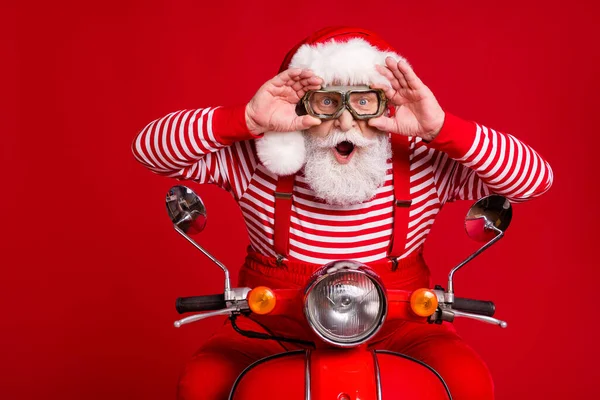 Zdjęcie funky emerytowany starzec motorower jeździć otwarte usta trzymać okulary niesamowite prędkości wiatr nosić Santa X-mas kostium szelki sunglass buty w paski koszula czapka odizolowany czerwony kolor tło — Zdjęcie stockowe