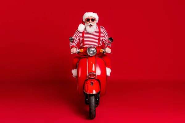 Pełna długość zdjęcie szalony emerytowany starzec motorower cieszyć się jeździć puste wietrzne autostrady otwarte usta nosić Santa X-mas kostium szelki sunglass buty w paski koszula czapka odizolowany czerwony kolor tło — Zdjęcie stockowe