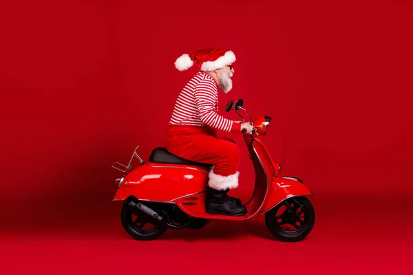 Pełna długość ciała rozmiar profil boczny widok jego przystojny brodaty Santa ojciec jazda motorowerem szybko dostarczając prezent North Pole podróżnik odizolowany jasny żywy połysk żywy czerwony kolor tło — Zdjęcie stockowe