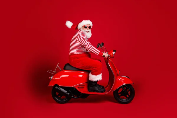 Pełna długość profil zdjęcie emerytowanego dziadka skuter jeździć autostradą szybkie beztroskie zużycie Santa x-mas kostium szelki sunglass buty w paski koszula czapka odizolowany czerwony kolor tło — Zdjęcie stockowe