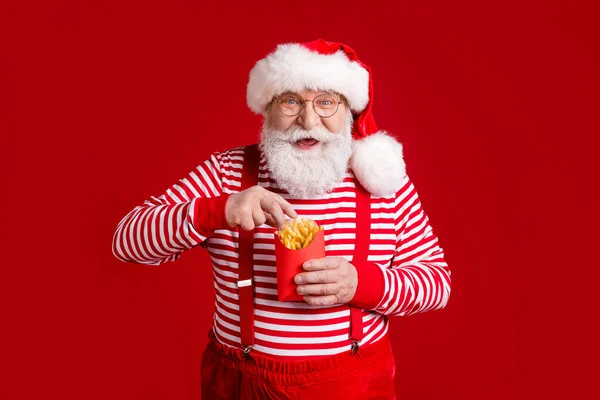 Portrait of his he nice handsome cheerful cheery hungry bearded Santa father eating fried delicious potato delivery lunch snack newyear isolated bright vivid shine vibrant red color background — Stock Photo, Image