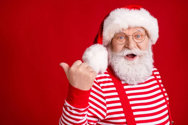 Zbliżenie zdjęcie emerytowanego dziadka biały broda bezpośredni palec pusty przestrzeń sugerują zimowy design nosić Santa x-mas stroje szelki okulary paski koszulka czapka izolowany czerwony kolor tło — Zdjęcie stockowe