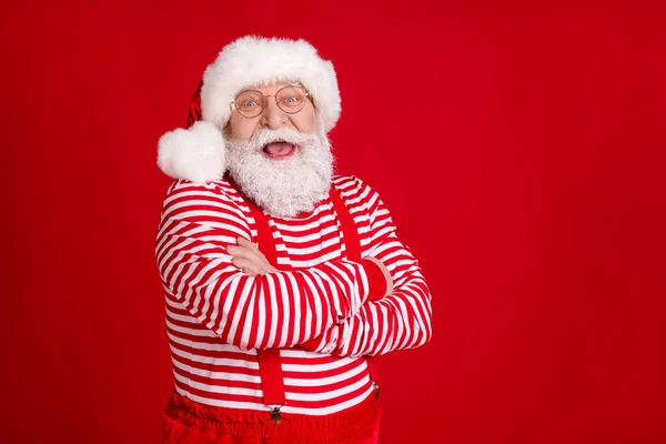 Profiel foto van gepensioneerde oude man gevouwen handen zelfverzekerde lege ruimte lach kind verhaal dragen kerstman kostuum bretels brillen gestreepte shirt hoofddeksel geïsoleerde rode kleur achtergrond — Stockfoto