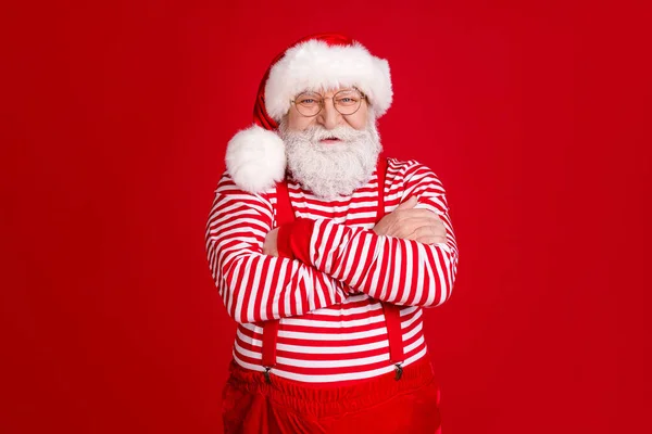 Foto di pensionato vecchio incrociato mani auto-assicurato nonno ascoltare i bambini auguri di Natale indossare bretelle costume occhiali camicia a righe copricapi isolato colore rosso sfondo — Foto Stock