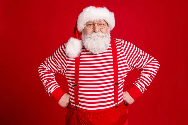 Foto de pensionista anciano manos caderas fresco abuelo preparar preguntar a los niños pregunta buen comportamiento desgaste traje de santa tirantes gafas rayas camisa diadema aislado color rojo fondo — Foto de Stock