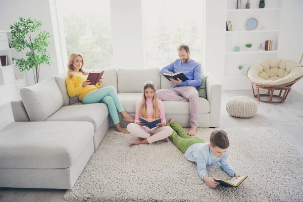 Pełne ciało zdjęcie skupione mama tata siedzieć kanapa dwa małe dzieci na podłodze czytać książki papieru w domu — Zdjęcie stockowe