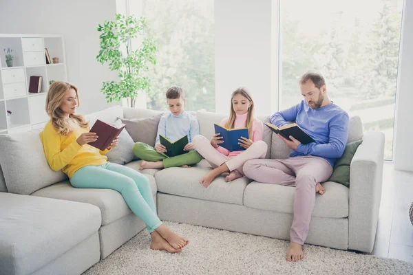 Foto de tamaño completo de la familia enfocada mamá papá dos niños niño niña sentarse sofá leer libro en casa en el interior — Foto de Stock
