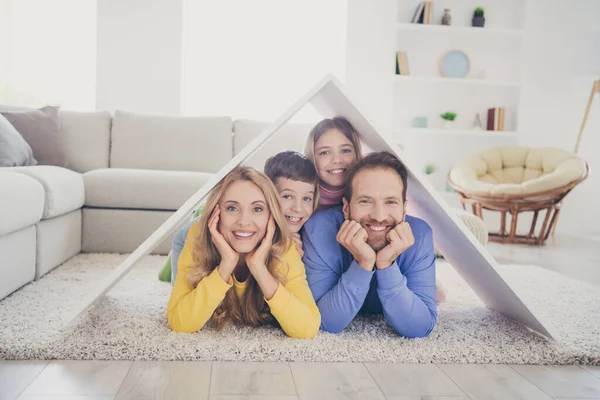 Säker familj nytt hus koncept. Foto av människor mamma pappa två små barn ligger golvet under papperskort tak i vardagsrummet inomhus — Stockfoto