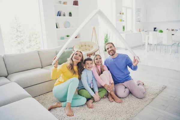 Volledige lichaam foto van harmonie familie mensen mama papa zitten vloer houden papieren kaart dak boven twee kleine kinderen in huis binnen — Stockfoto