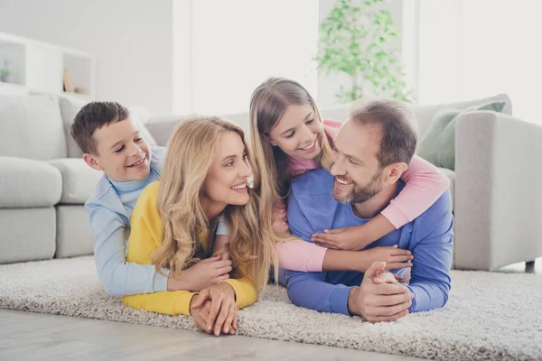 Foto av charmig mamma pappa liggande matta grepp piggyback två bedårande små barn flicka pojke i huset inomhus — Stockfoto