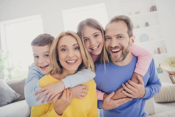 Photo of idyllic family mom dad hug piggyback two adorable kids boy girl in house indoors — Stock Photo, Image