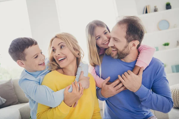 Foto av idylliska mamma pappa kram piggyback två små barn på familjesemester i hus inomhus — Stockfoto