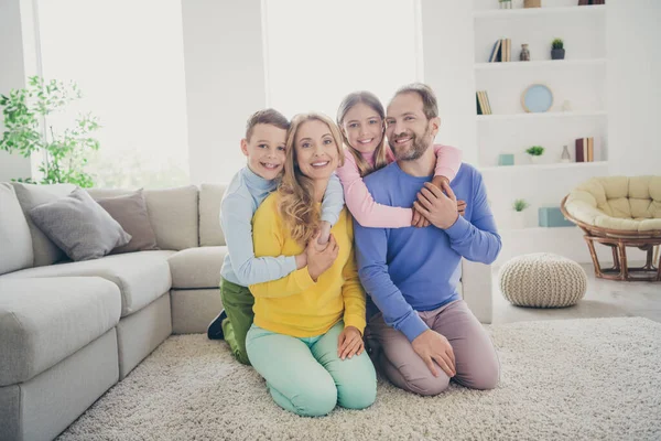 Fin de semana familiar positivo. Foto de tamaño completo de mamá papá abrazo a cuestas dos niños niño niña sentarse piso en casa en el interior — Foto de Stock