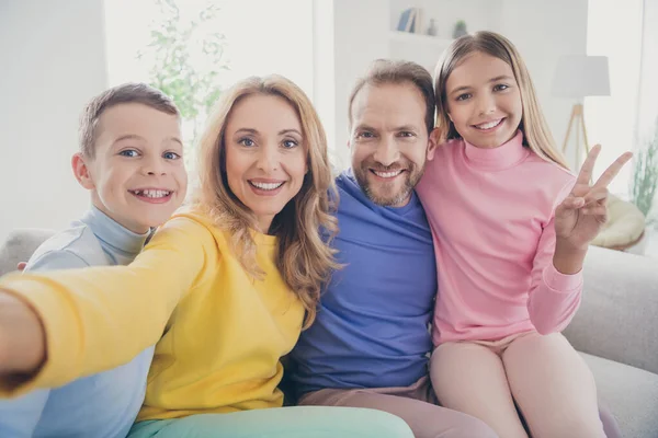 Foto de familia positiva sentarse sofá mamá tomar selfie niña hacer v-signo con el hermano y el papá en la casa en el interior — Foto de Stock