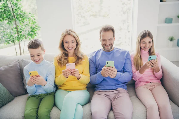 Foto de cuerpo completo de la gente positiva de la familia sentarse sofá mamá papá dos niños pequeños utilizan el teléfono inteligente en casa en el interior —  Fotos de Stock