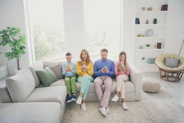 Volledige lengte foto van familie zitten bank mam vader en twee kleine kinderen jongen meisje gebruik smartphone lees nieuws in huis binnen — Stockfoto