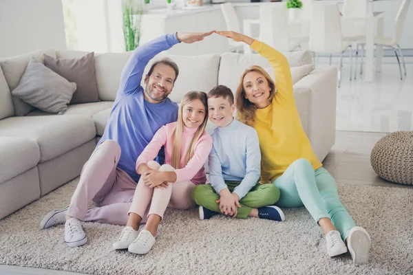 Фотографія ідилічних людей сім'я сидить на підлозі мама тато тримає руки вище двох маленьких дітей в будинку в приміщенні — стокове фото