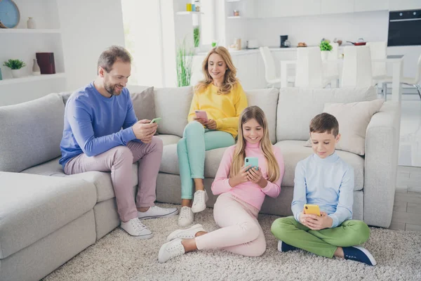 妈妈爸爸和两个小孩在智能手机上发短信的全长照片坐在屋里沙发地板上 — 图库照片