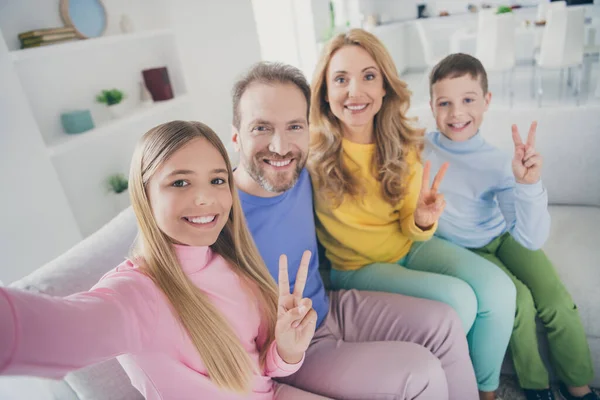 Foto van positieve mensen familie zitten bank moeder vader twee kleine kinderen maken v-teken nemen selfie in huis binnen — Stockfoto