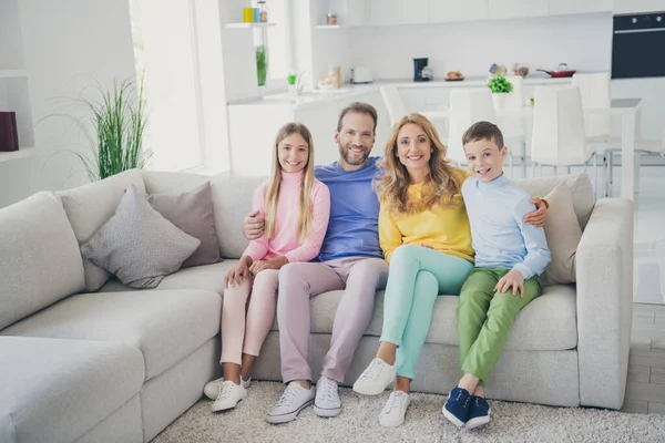 Фотографія повного тіла позитивної сім'ї сидить на дивані тато обіймає маму і двох дітей дівчинка-хлопчик в будинку в приміщенні — стокове фото