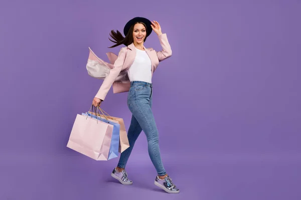 Full length photo positive girl shopping center client hold many bags her hair fly air wind she touch hand headwear wear beige spring outfit denim jeans shoes isolated violet color background — Stock Photo, Image