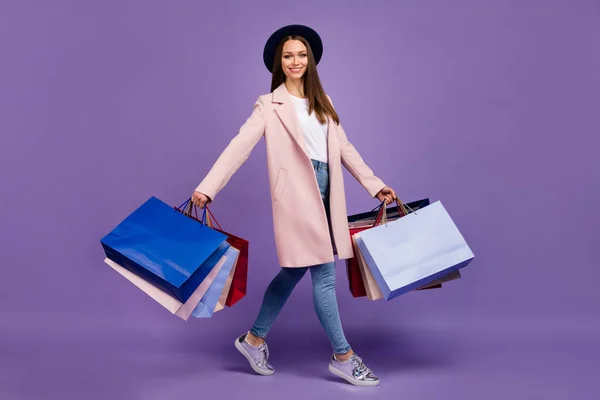 ショッピングモールから行く多くのバッグを保持している陽気な素敵なトレンディーな女の子の完全な長さのプロフィール側の写真ベージュの服のデニムのヘッドウェアのスニーカーは紫の色の背景に隔離 — ストック写真