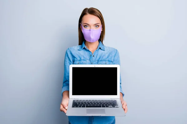 Retrato fotográfico de la mujer sosteniendo el ordenador portátil con espacio en blanco usando mascarilla de tela púrpura aislada sobre fondo de color blanco — Foto de Stock