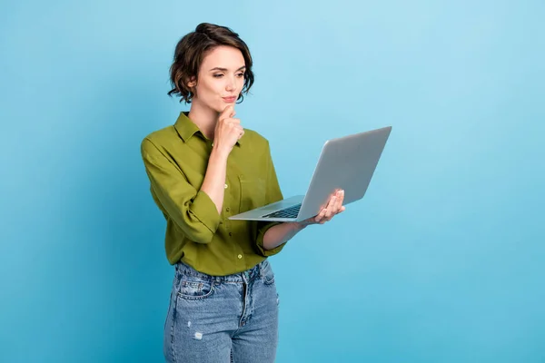 Photo of charming lady short hairdo hold netbook palec podbródek wygląd ekran nosić jeansy zielony koszula odizolowany niebieski kolor tło — Zdjęcie stockowe