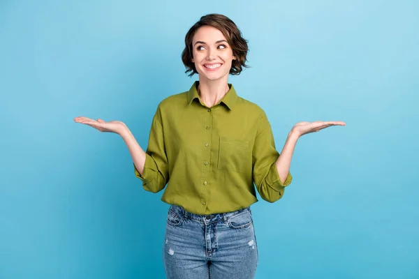 Foto de linda senhora bonito penteado curto olhar lado segurar duas mãos espaço vazio toothy beaming sorriso desgaste jeans camisa verde isolado azul cor fundo — Fotografia de Stock