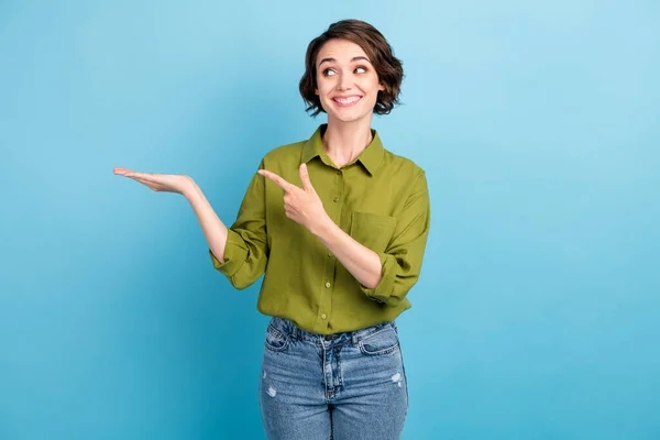 Foto de muito bonito senhora penteado curto engraçado interessado olhar direcionando dedo segurar mão espaço vazio desgaste jeans verde camisa isolado azul cor fundo — Fotografia de Stock