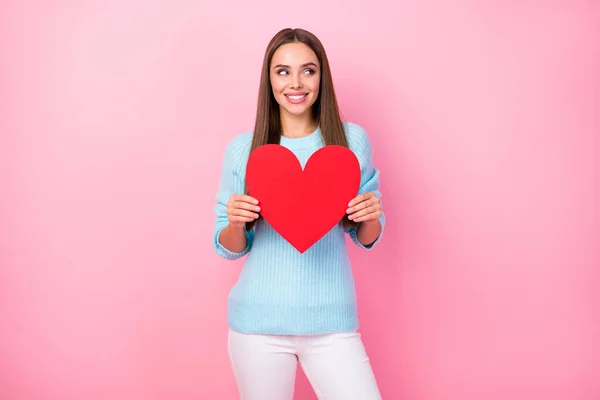 Foto av söt dam hålla papper rött hjärta kreativt vykort bjuda pojkvän romantik datum blyg att titta ögon bära stickad blå tröja vita byxor isolerad pastell rosa färg bakgrund — Stockfoto