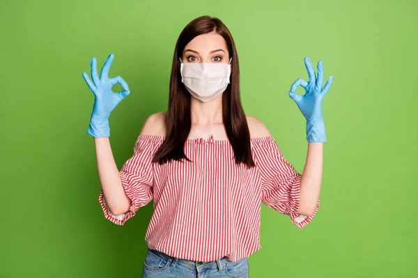 Φωτογραφία του κοριτσιού στην ιατρική μάσκα δείχνουν εντάξει σημάδι εγκρίνει covid προστασία της υγιεινής φορούν καουτσούκ μπλε γάντια λάτεξ κόκκινα λευκά ρούχα απομονώνονται σε πράσινο χρώμα φόντο — Φωτογραφία Αρχείου