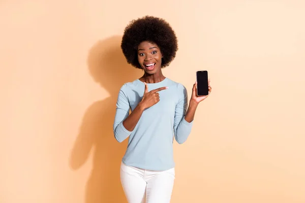 Foto portret van jonge brunette Afrikaanse Amerikaanse vrouw met mobiele telefoon met copyspace wijzen een vinger geïsoleerd op pastel beige gekleurde achtergrond — Stockfoto