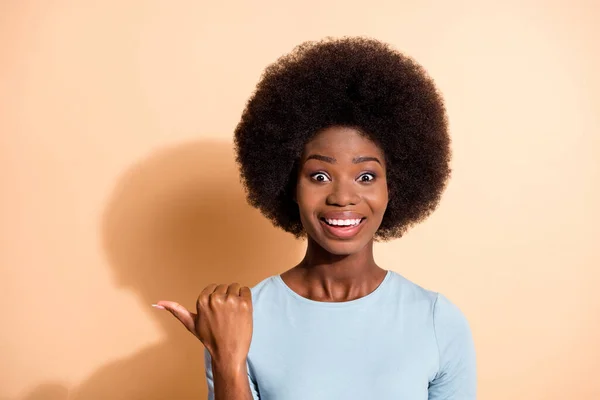 Fotoporträt eines aufgeregten afrikanisch-amerikanischen Mädchens, das mit dem Daumen auf eine Leerstelle zeigt, isoliert auf pastellbeigem Hintergrund — Stockfoto