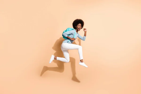 Foto retrato de morena afro-americana correndo pulando usando roupas casuais saco ciano isolado no fundo de cor bege pastel — Fotografia de Stock